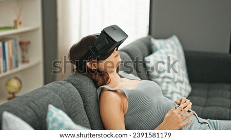 Young beautiful hispanic woman playing video game using virtual reality glasses at home