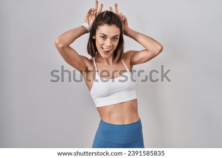Hispanic woman wearing sportswear over isolated background posing funny and crazy with fingers on head as bunny ears, smiling cheerful 
