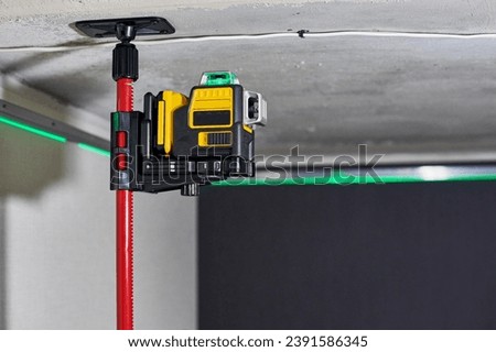 Laser level measuring tool with visible green laser beam on wall at unfinished apartment. Professional equipment for installing stretch ceiling. Home renovation concept, close up Royalty-Free Stock Photo #2391586345