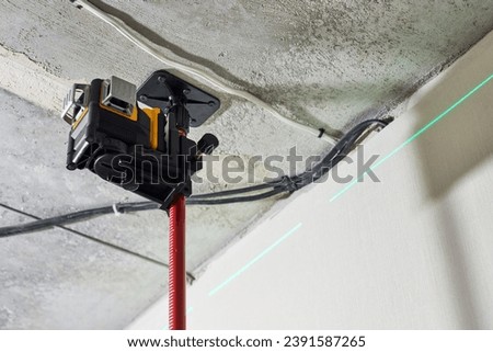 Laser level measuring tool with visible green laser beam on wall at construction site. Measuring level. Professional equipment for installing stretch ceiling. Home renovation concept, close up Royalty-Free Stock Photo #2391587265