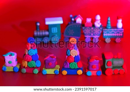 A toy Christmas train made of plasticine with gifts and Christmas trees. Bright red background. New Year decorations.