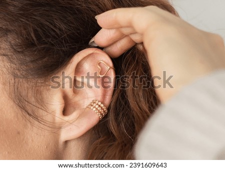 Cropped close-up shot of a young woman with two asymmetrical golden ear cuffs. Female with golden ear cuffs, side view Royalty-Free Stock Photo #2391609643