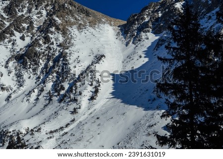 Mountain couloir with snow and ice for freestyle skiing or snowboarding among dark rocks on a clear frosty day