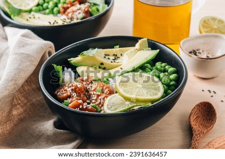 Buddha bowl with crispy sesame chicken asian style. Sweet and sour fried chicken with steamed rice, peas and acocado on light wooden background. Healthy and balanced food concept. Selective focus Royalty-Free Stock Photo #2391636457