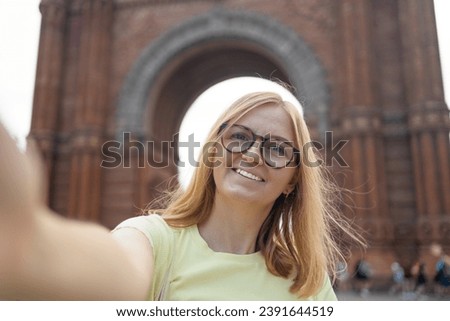 Happy woman travel take a photo or video of Arc de Triomf in Barcelona under blue sky. High quality photo