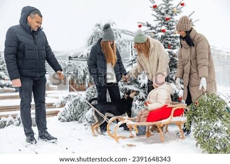 Outdoor portrait of happy big European family in warm clothes with a dog spending time actively in winter snowy backyard at home, parents with children posing against snow-covered Christmas tree