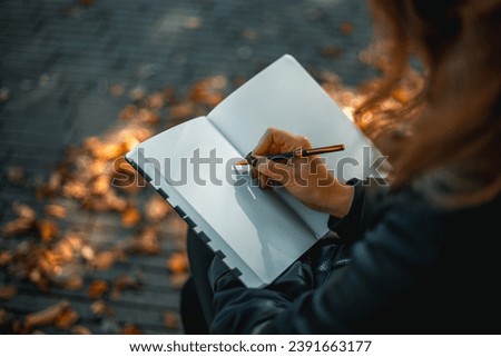 Close up portrait of a relaxed young girl writing a book while sitting on a bench. International Writers' Day