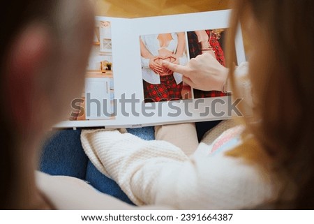 mother and daughter flips through a photo book with photos of dad and pregnant mom. Beautiful memory. Professional photo printing. services of photographer and designer. original gift for the family. Royalty-Free Stock Photo #2391664387