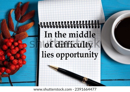 IN THE MIDDLE OF DIFFICULTY LIES OPPORTUNITY - words in a white notebook on a wooden blue background with a rowan branch and a fragment of a cup of coffee. Medical concept