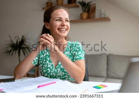 Inspired and motivated adult student woman laughs while doing homework at home sitting at the desk.