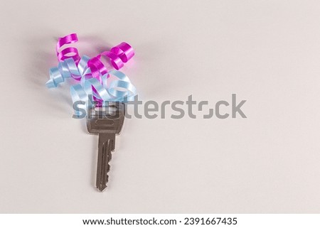 Key with pink and blue ribbon on a white surface. Place for text.
