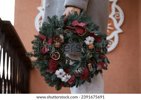 Woman holds creative Christmas wreath outdoor. Preparing for Christmas.