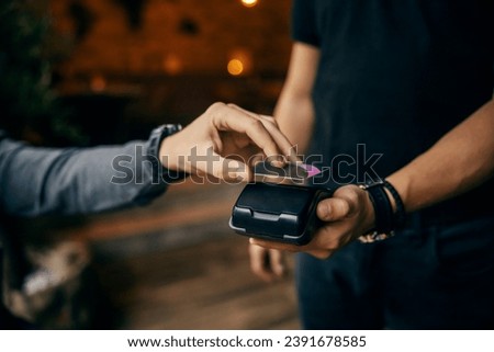 Cropped picture of a male's hand using credit card on POS machine ion cafe.