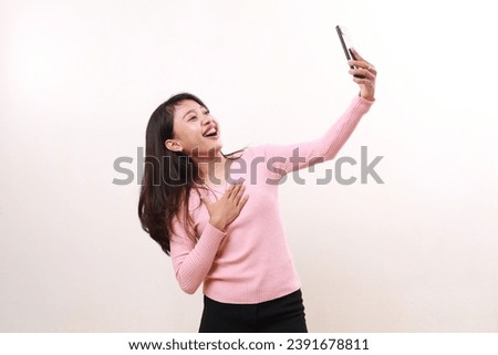 Cheerful young asian girl standing while doing selfie. Isolated on white background