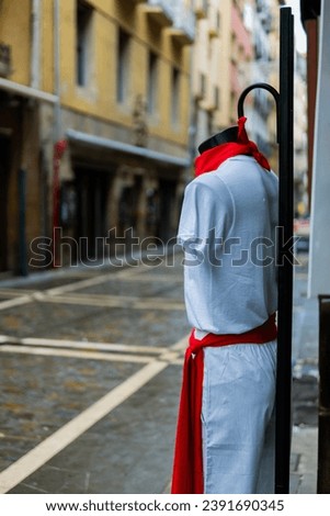 Traditional outfit mannequin stands alone, white-red attire, empty pedestrian street cloudy Pamplona