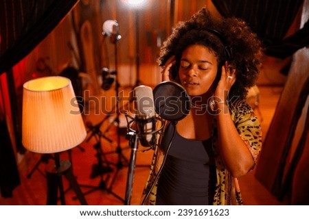 A talented young vocalist with curly hair is singing from the heart into a condenser microphone, recording a track in a music studio. Alternative, fashionable, soul music, indie.