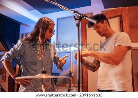 A young talented music producer talking to his assistant in a stylish minimalist recording studio. He is pointing to a piece of equipment the assistant is holding with both hands.