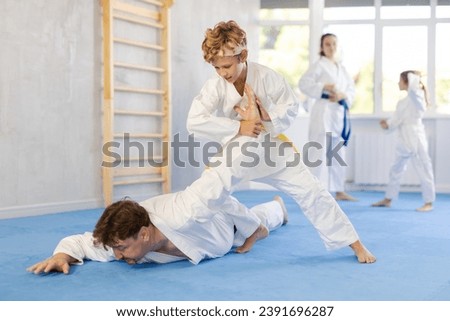 Determined preteen boy practicing armlock, painful control move to hold and immobilize opponent, in training bout with father during martial arts course in gym Royalty-Free Stock Photo #2391696287