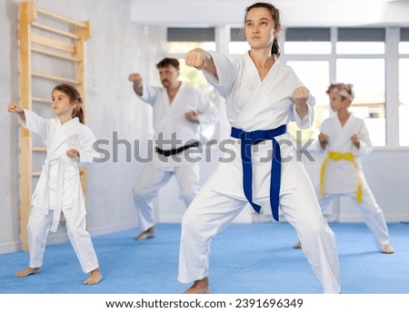 Experienced female karateka demonstrating kata sequence of movements to preteen daughter and son emphasizing hand striking techniques during family martial arts training .. Royalty-Free Stock Photo #2391696349