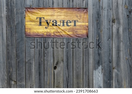 Rustic Toilet sign, written in Russian, on weathered wooden boards
