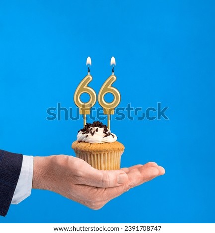 Hand delivering birthday cupcake - Candle number 66 on blue background Royalty-Free Stock Photo #2391708747