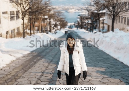 Woman tourist Visiting in Hakodate, Traveler in Sweater sightseeing Hachiman Zaka Slope with Snow in winter. landmark and popular for attractions in Hokkaido, Japan. Travel and Vacation concept