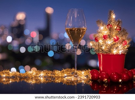 A glass of white wine that have Christmas ornament decoration put on table with city bokeh light background. Christmas dining concept.