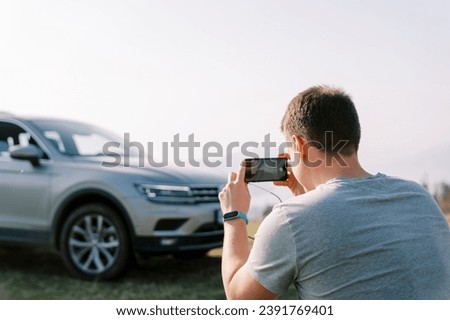 Driver takes a picture of his car on a green lawn with a smartphone. Back view