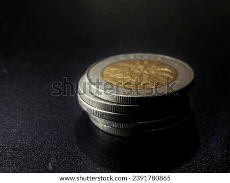 A pile of ancient Indonesian coins with a nominal value of 1000 rupiah. Dark background. Blurred background. Selective focus, soft focus, macro mode. Royalty-Free Stock Photo #2391780865