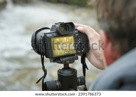 Photographer at work holding a digital camera and taking pictures of a landscape. Nature and people in work scene.