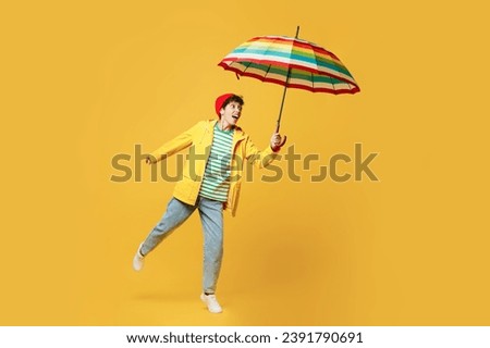 Full body young happy woman wears waterproof raincoat outerwear red hat hold run with umbrella isolated on plain yellow background studio portrait. Outdoors lifestyle wet fall weather season concept