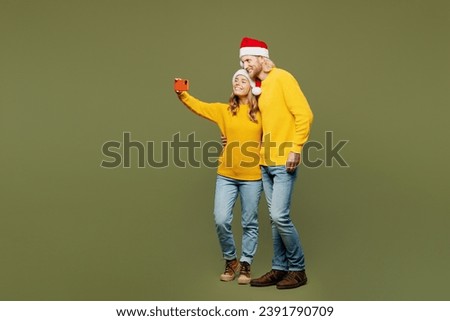 Full body merry young couple two friends man woman wear sweater Santa hat posing doing selfie shot on mobile cell phone hug isolated on plain green background. Happy New Year Christmas holiday concept