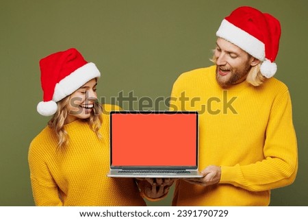 Merry fun young couple two IT friends man woman wear sweater Santa hat posing work use laptop pc computer blank screen area isolated on plain green background. Happy New Year Christmas holiday concept