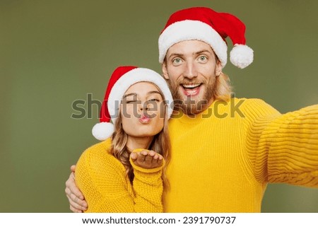 Close up young couple two friends man woman wear sweater Santa hat posing do selfie shot on mobile cell phone blow air kiss isolated on plain green background. Happy New Year Christmas holiday concept