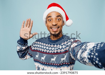Close up young man wears sweater Santa hat posing doing selfie shot pov on mobile cell phone waving hand isolated on plain blue background. Happy New Year 2024 celebration Christmas holiday concept