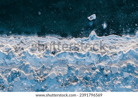 Top view of the freezing sea. Winter aerial photograph of the icy coast and ice floes in sea water. Nature of the Extreme North. Cold frosty winter weather. Harsh arctic climate. Natural background. Royalty-Free Stock Photo #2391796569