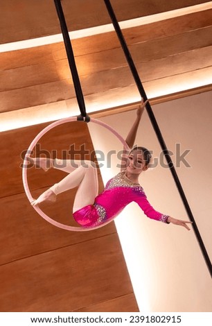 Asian gymnast girl doing gymnastics performance on aerial hoop in fitness gym. Female acrobat doing acrobatic and flexible tricks on aerial ring (lyra) in photo studio  Royalty-Free Stock Photo #2391802915