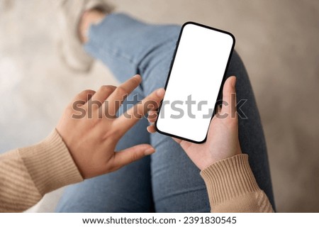 A woman using her smartphone while sitting indoors. A white-screen smartphone mockup. touching screen, using a mobile app, texting, scrolling on social media