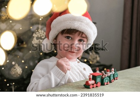 Portrait of a cute two year old boy in a Santa hat on the background of a Christmas tree