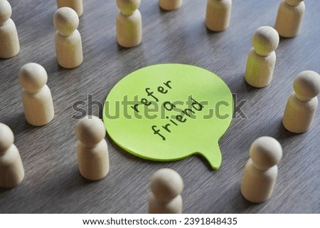 Closeup image of speech bubble with text REFER A FRIEND surrounded by a group of wooden dolls.  Royalty-Free Stock Photo #2391848435