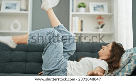 Young beautiful hispanic woman smiling lying on the sofa moving legs at home