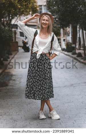 Smiling young beautiful woman in a stylish image of a tourist holds a hat with her hand in the middle of a beautiful historical street, Turkey. Concept of travel, lifestyle. Vertical photo