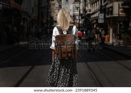 Portrait from the back of a young female tourist in a white shirt, skirt and a craft backpack on a popular street in Istanbul on a sunny day. Royalty-Free Stock Photo #2391889345