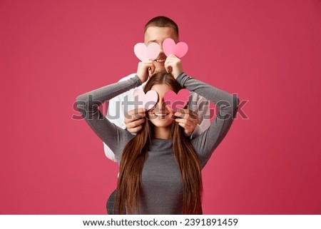 Young man and woman, beautiful couple celebrating holiday, posing with hearts against pink studio background. Concept of love, relationship, Valentine's Day, emotions, lifestyle