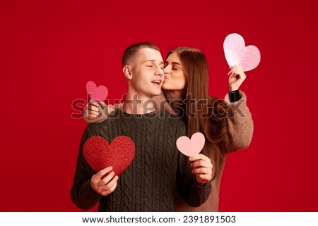 Portrait of beautiful, happy young couple, man and woman posing, having fun against red studio background. Concept of love, relationship, Valentine's Day, emotions, lifestyle