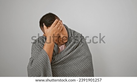 Freezing young latin man wrapped in cozy blanket, braving winter cold indoors, comfort against white isolated background, possibly ill Royalty-Free Stock Photo #2391901257