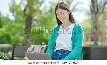 Young chinese woman using laptop sitting on bench at park