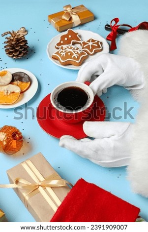 Santa Claus hands with cup of coffee, treats and Christmas gifts on color background, closeup