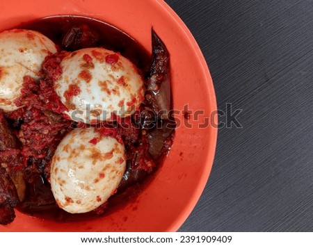 Round egg red chili sauce and purple eggplant in a small bowl. There is a lot of oil around the food, making it unhealthy for the body. picture with black background