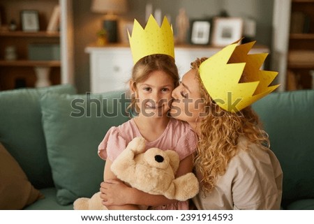 A portrait of little girl and mother with paper crowns having fun at home
